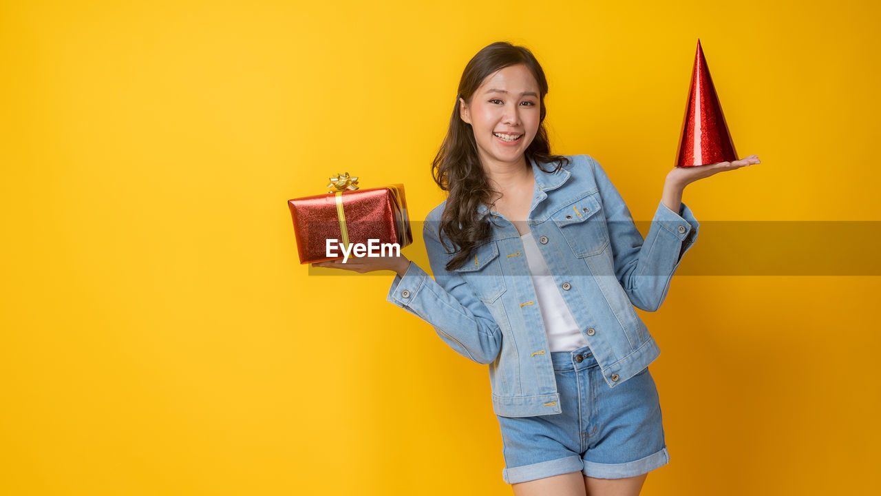 PORTRAIT OF A SMILING YOUNG WOMAN AGAINST YELLOW COLORED BACKGROUND