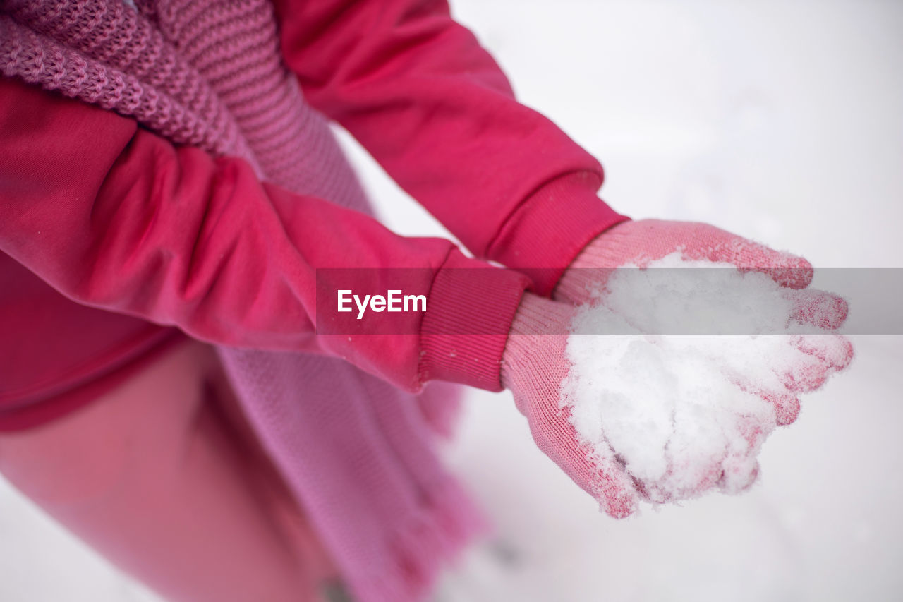 Woman in pink clothes gloves pants jacket holds snow in her hands