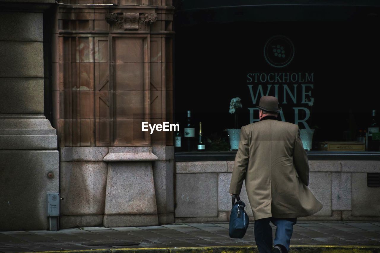 REAR VIEW OF A MAN WALKING ON STREET