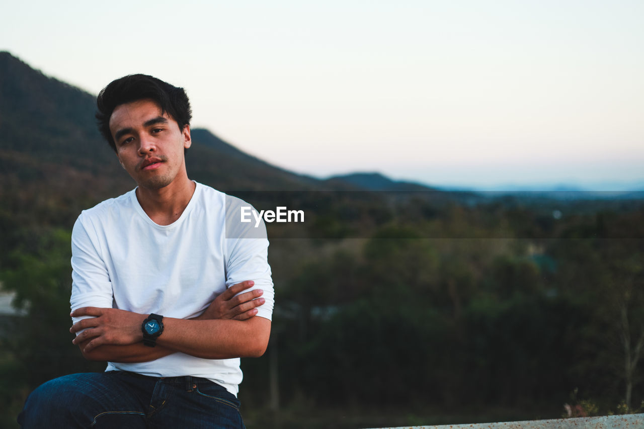 Portrait of young man sitting against mountains