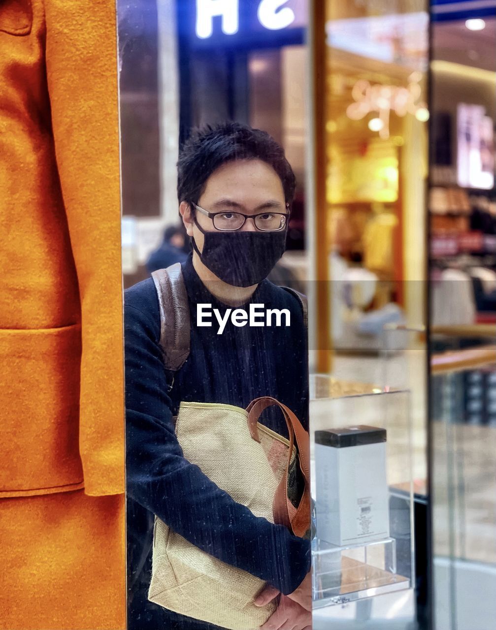 Portrait of young man standing reflected in mirror at shopping mall.