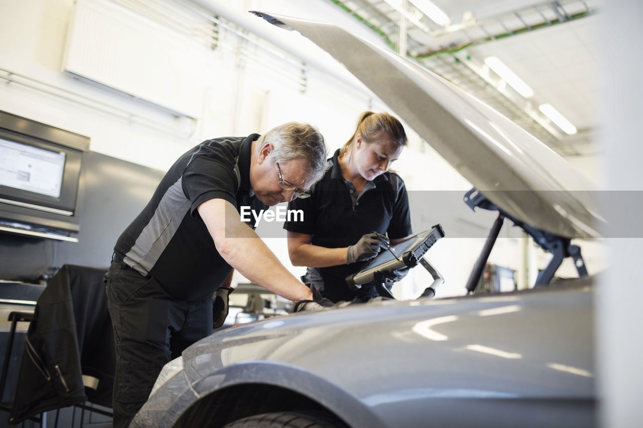 Male and female technicians examining car at shop