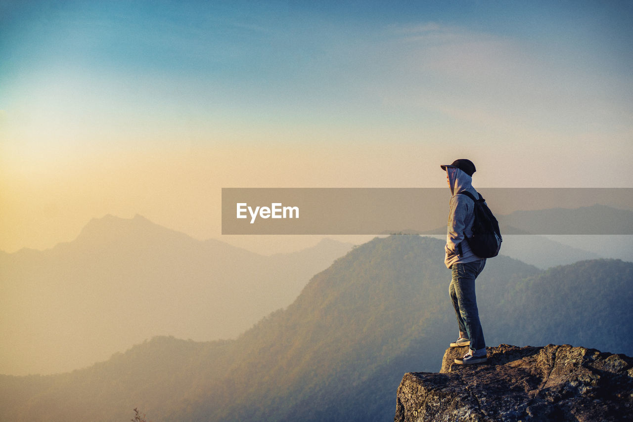 Side view of man standing on rock against sky