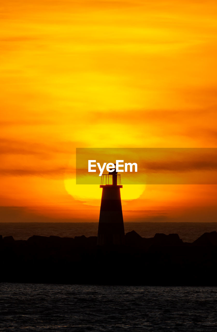 Large sun behind a silhouette lighthouse during a fiery sunset