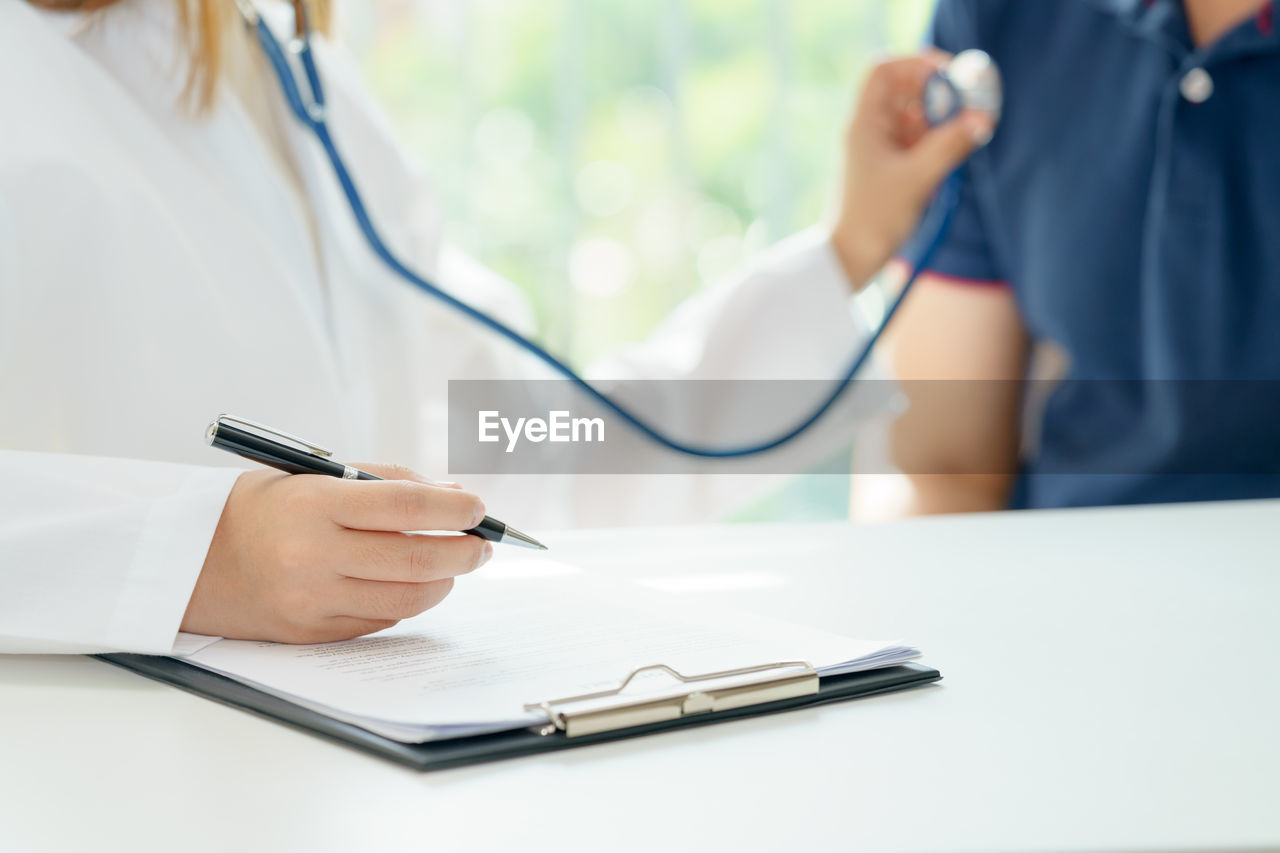 Midsection of female doctor examining patient with stethoscope in clinic