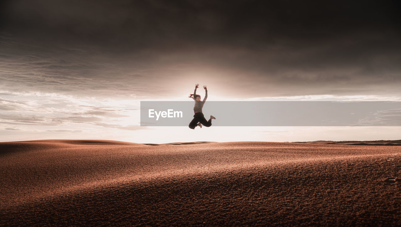 Women jumping on sand dunes against sky