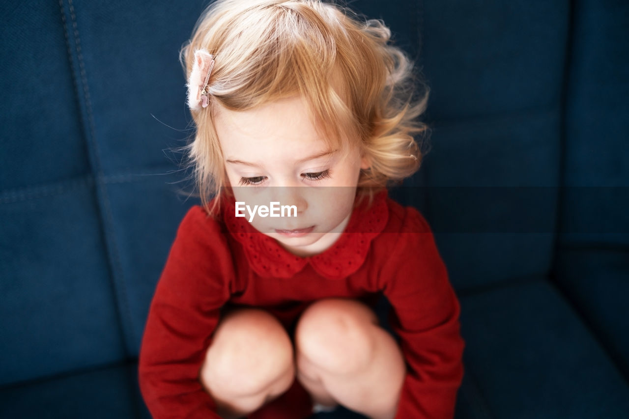 Sad cute baby girl, toddler with blond curly hair hugging knees to chest.kid, child bad mood