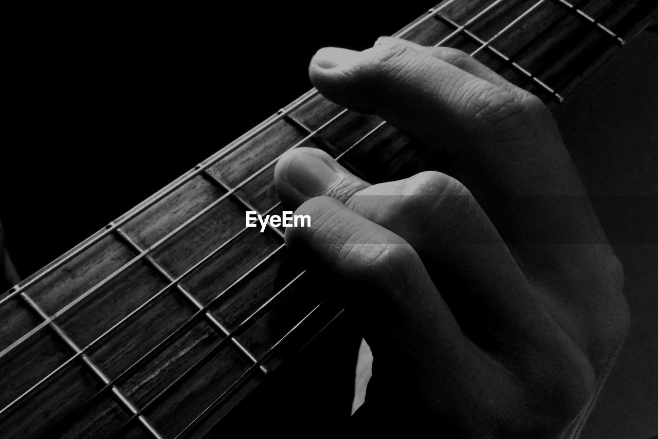 Close-up of hands playing guitar against black background