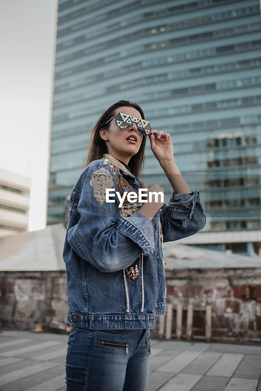 Young woman wearing sunglasses while standing against building in city