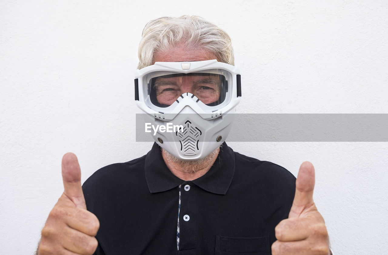 Portrait of senior man wearing mask standing against wall