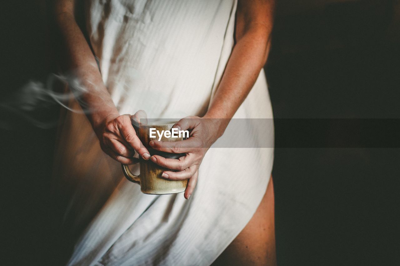 Midsection of woman holding coffee over black background