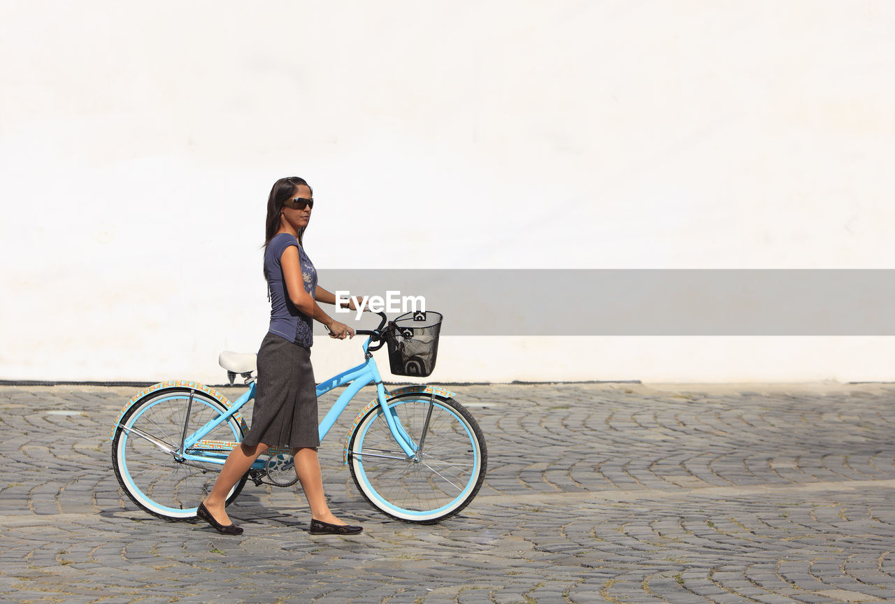 Woman with bicycle walking on footpath against wall