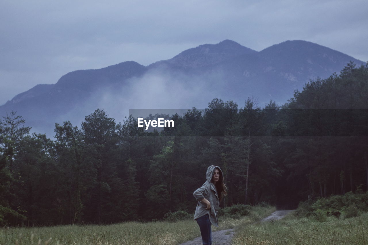 Side view of woman standing on field against mountain during dusk