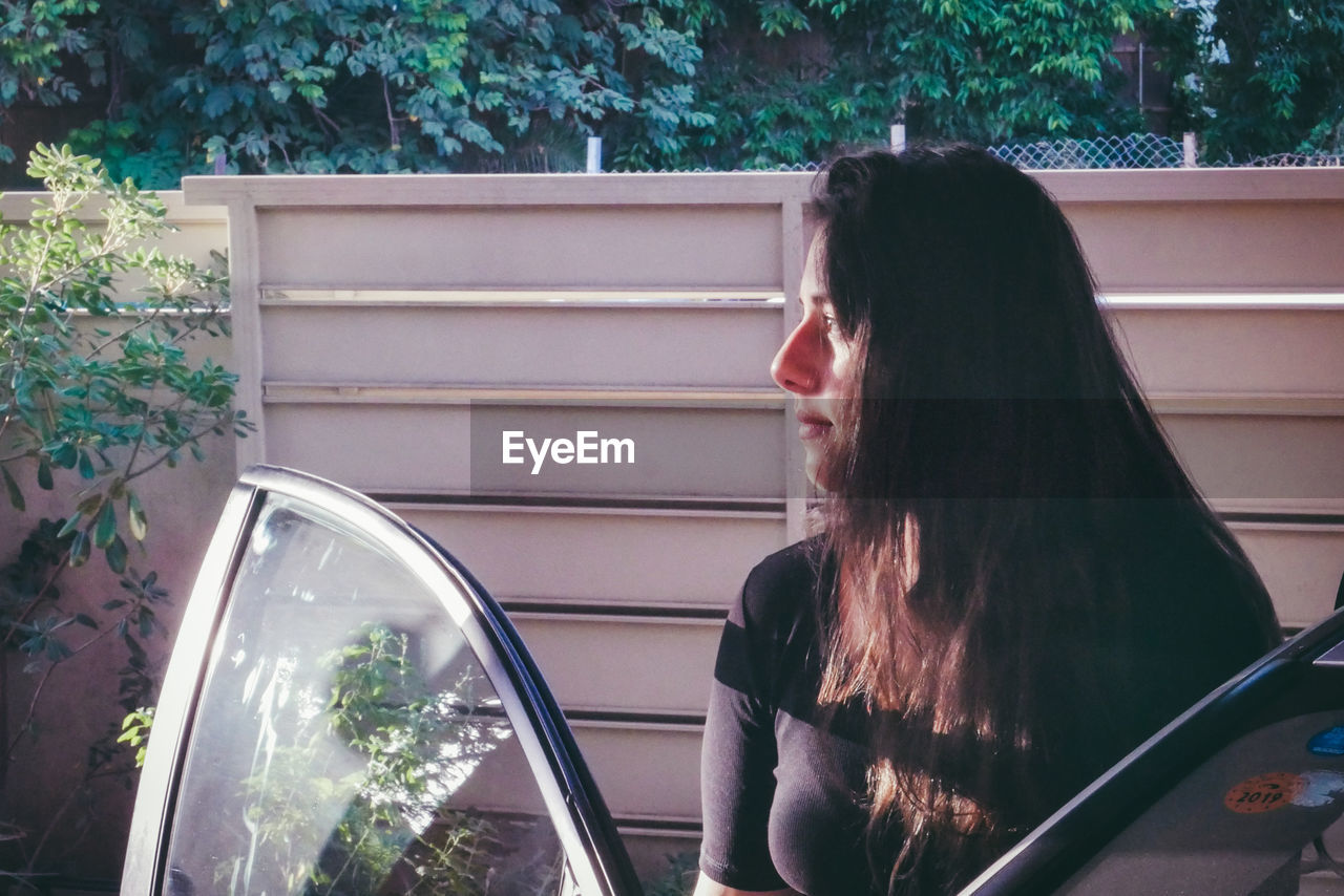 Thoughtful young woman looking away by car