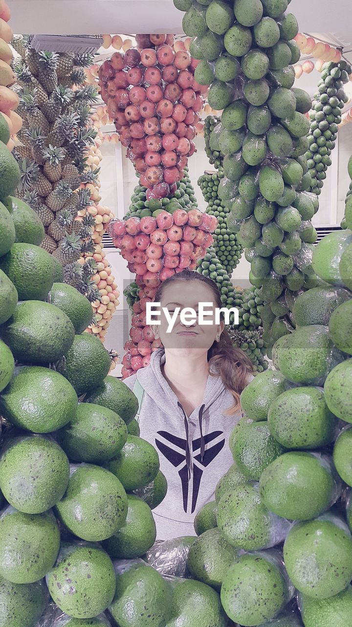 Young woman seen through avocados for sale at market