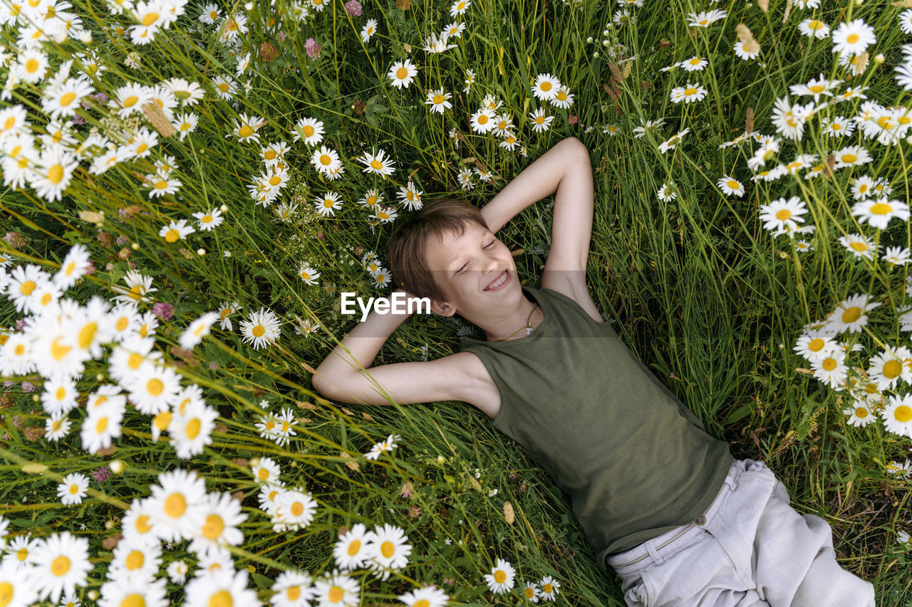 Smiling boy with hands behind head lying on chamomile plants in field