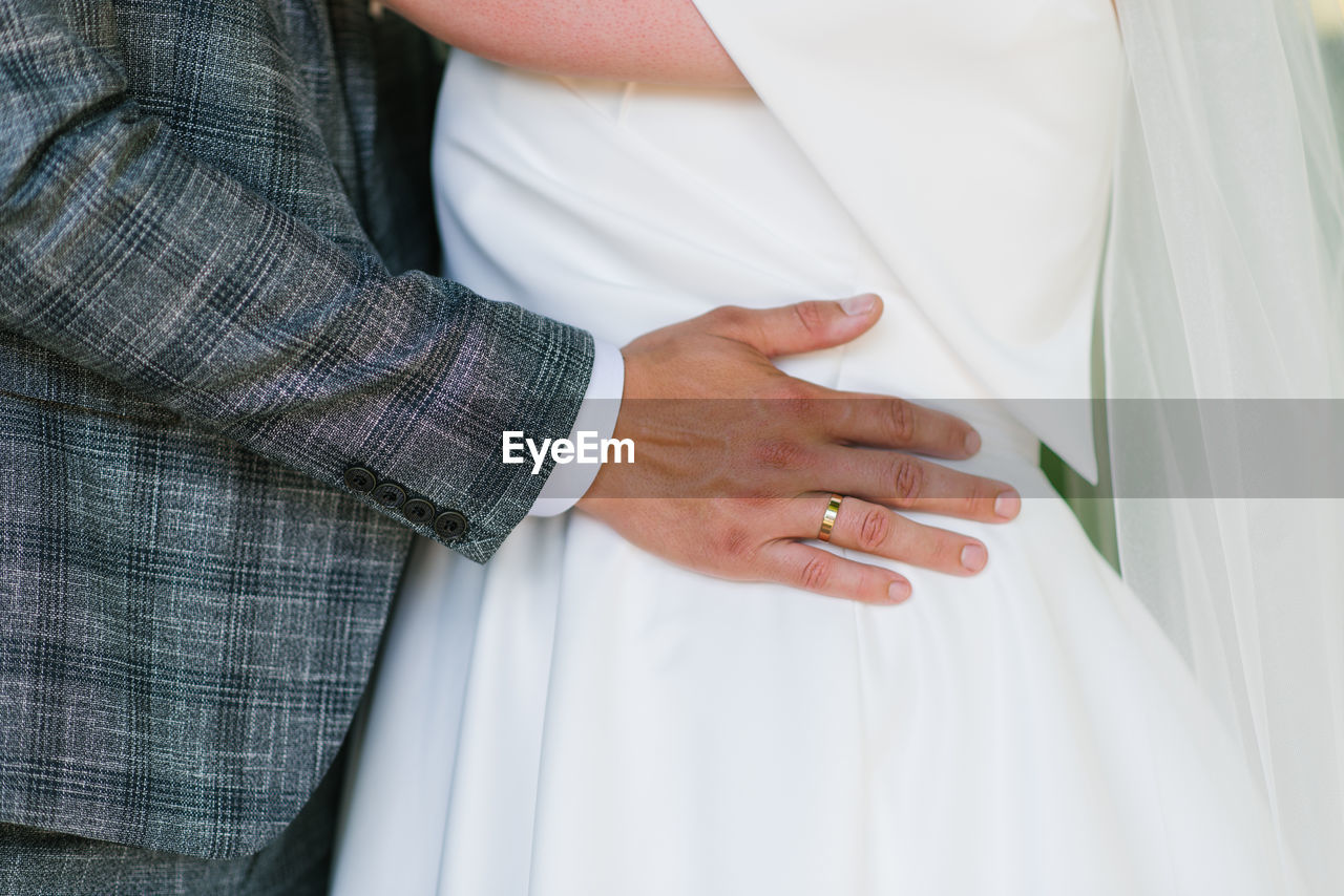 Groom's hand with the wedding ring lies on the bride's waist person