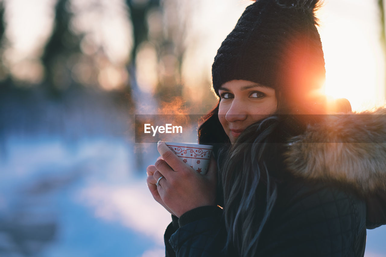 Side view portrait of woman wearing warm clothing holding hot drink in winter