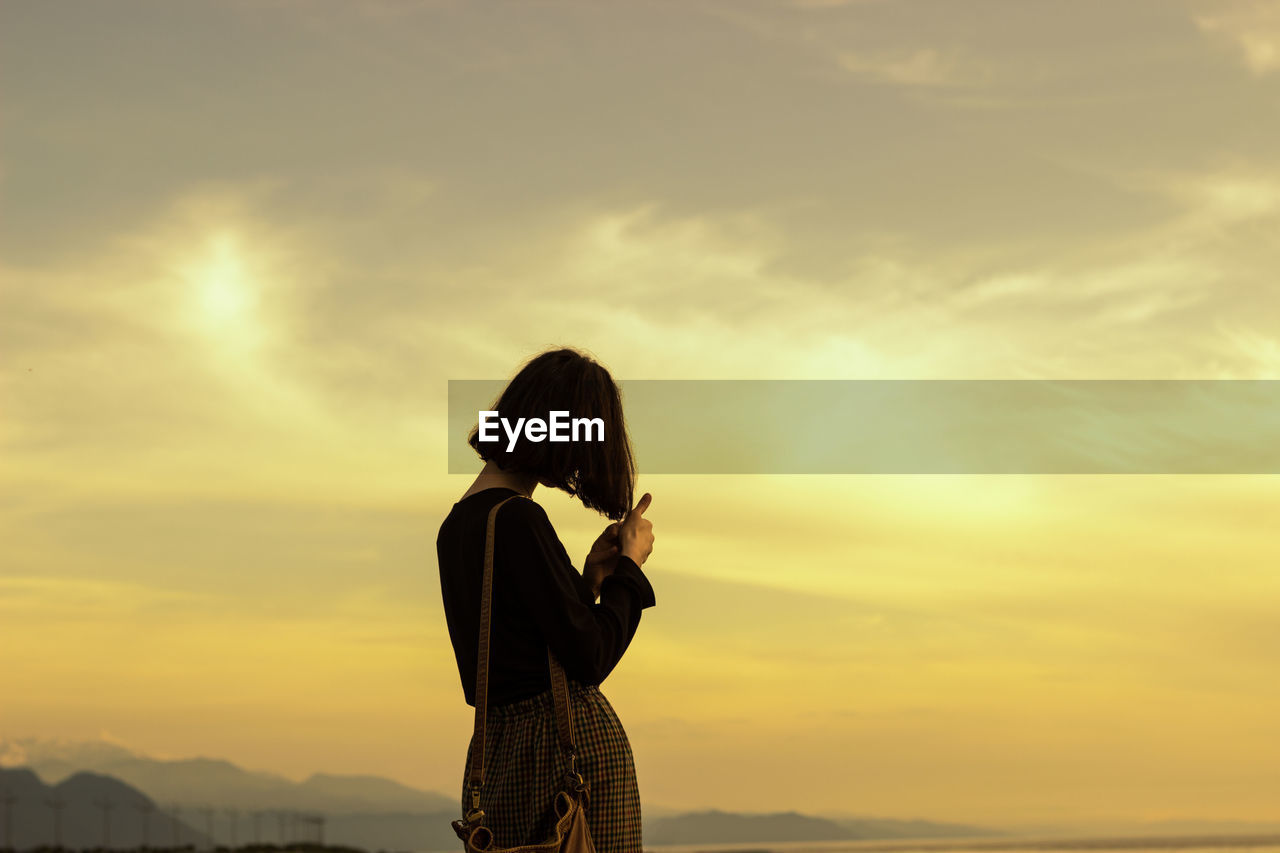 Silhouette of woman standing against sky during sunset