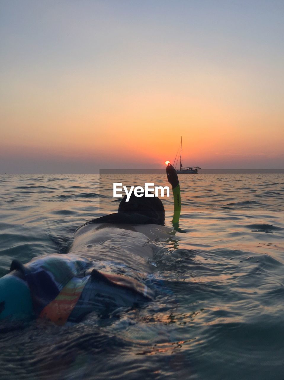 Rear view of man swimming in sea against sky during sunset