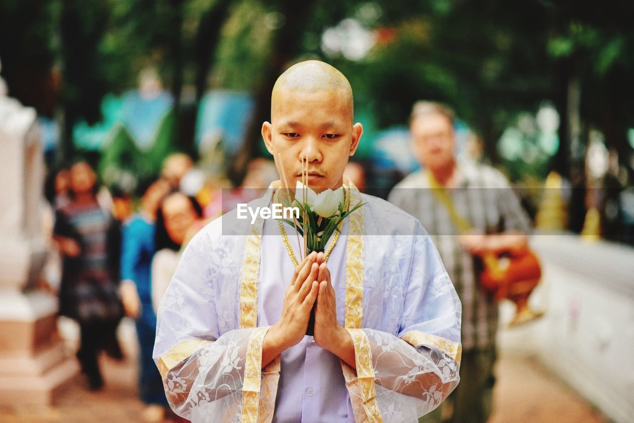 Portrait of monk holding flowers while praying
