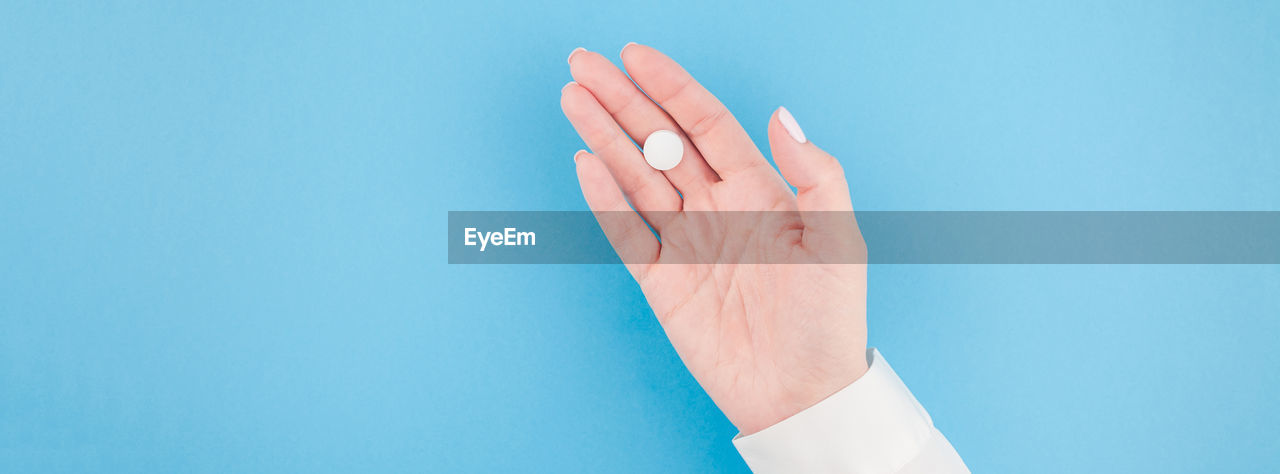 Close-up of person hand holding pill against blue background