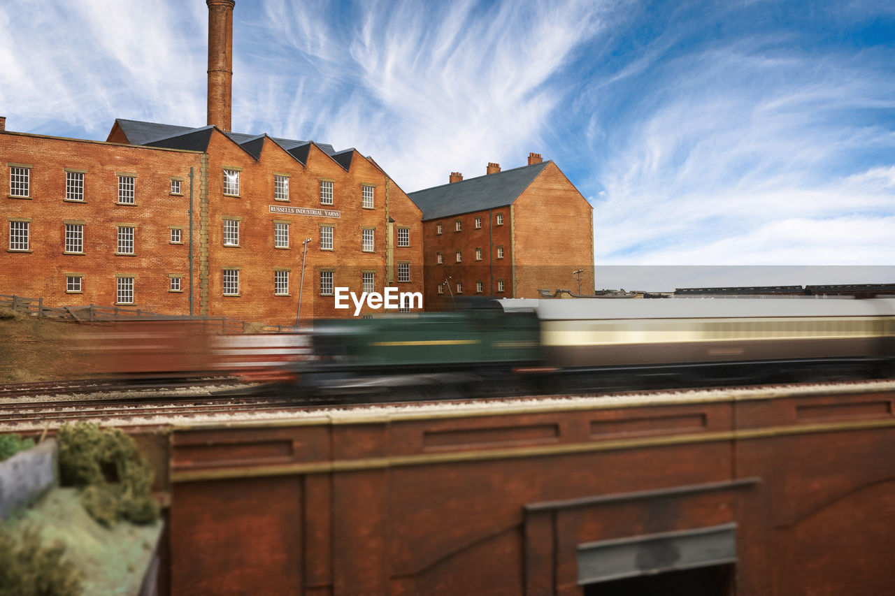 Side view of speeding blurred train against buildings