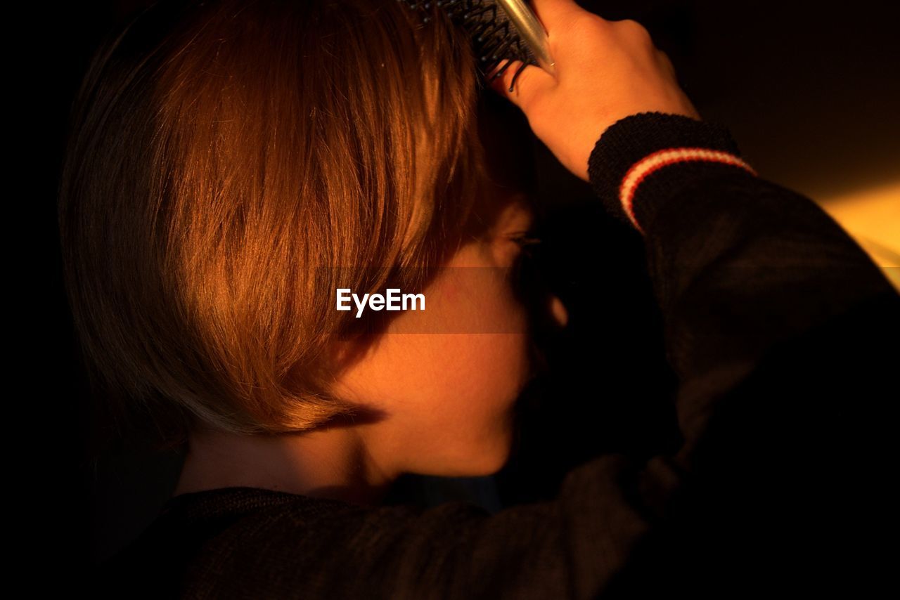 Close-up of boy combing hair in darkroom at home