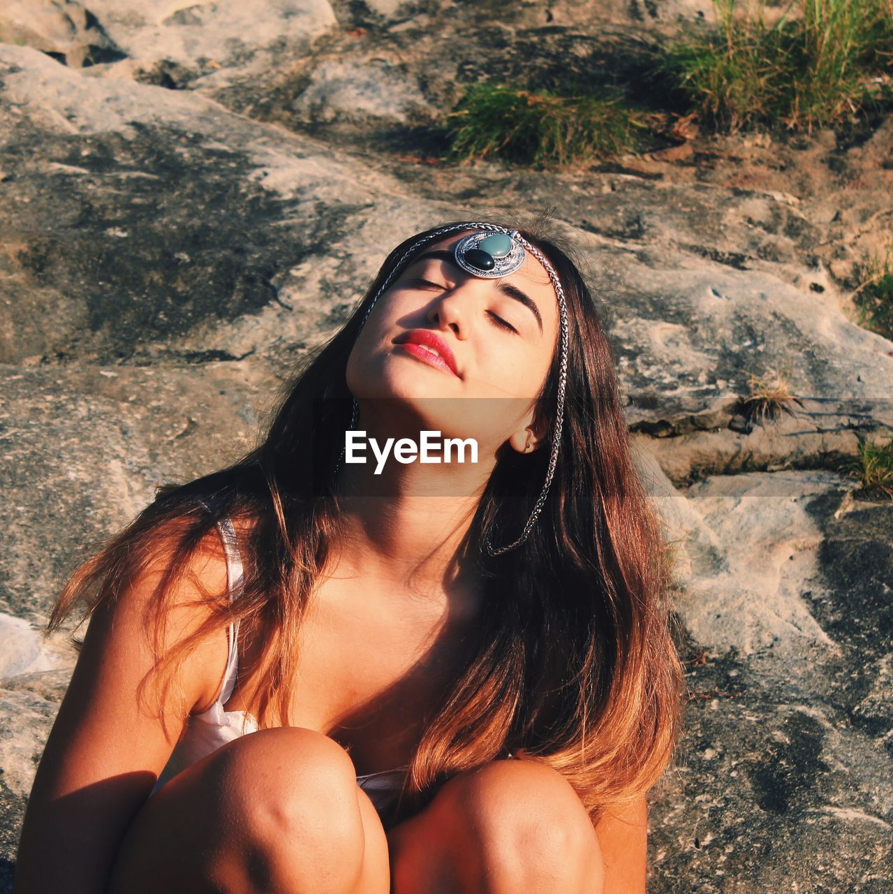 Young woman with pendant on forehead and eyes closed sitting on rock