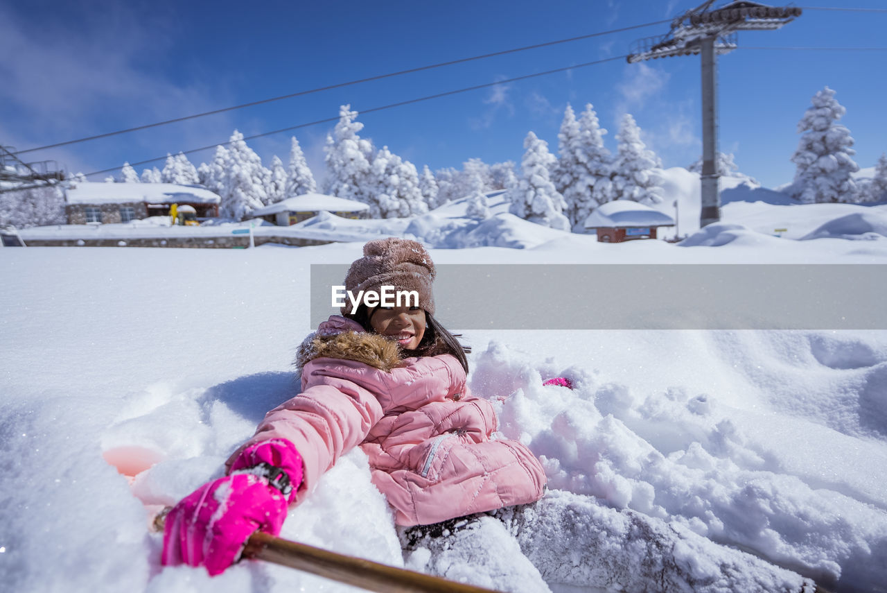 full length of girl sitting on snow covered field against sky