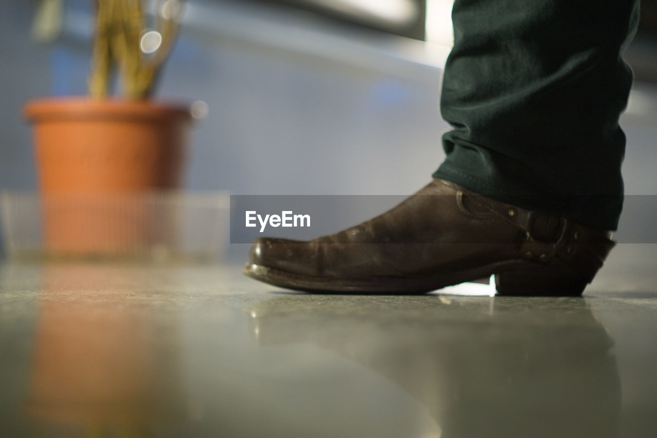 LOW SECTION OF MAN WEARING SHOES STANDING ON FLOOR