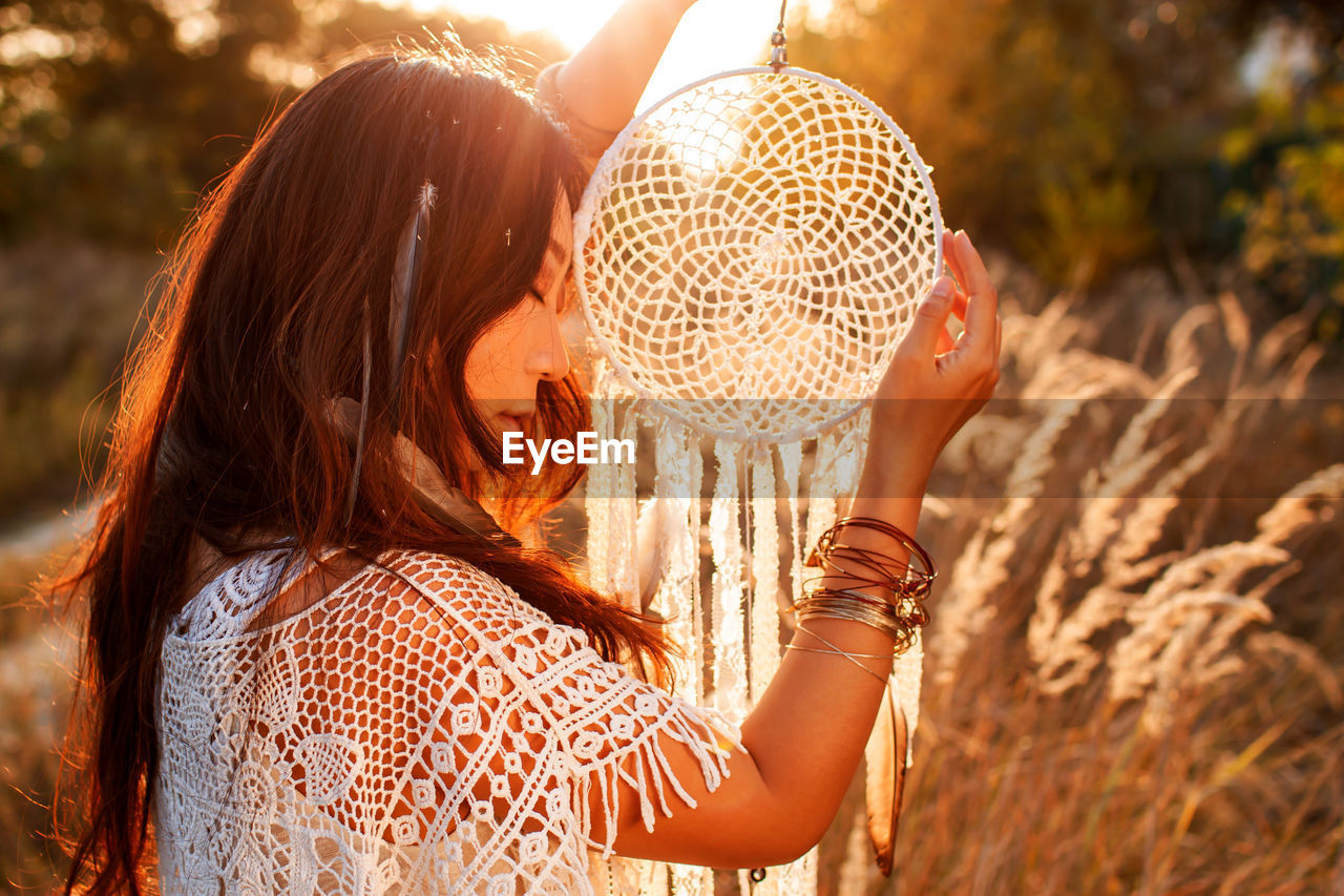 Asian girl holding dream catcher at sunset in field