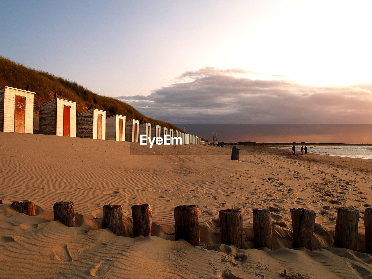 Wooden posts and beach huts on sea shore against sky during sunset