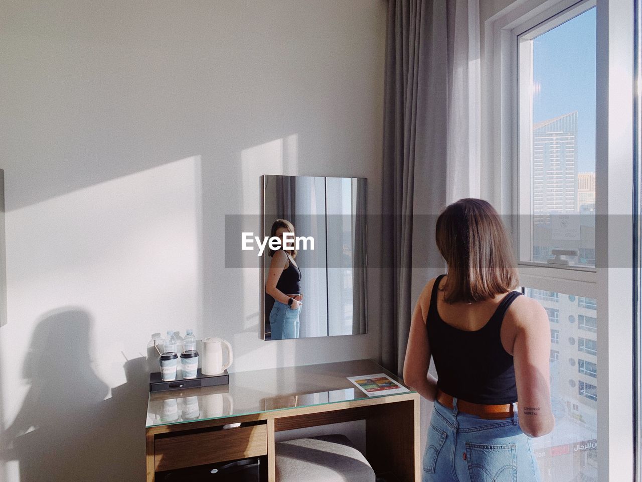 Side view of young woman looking through window at home