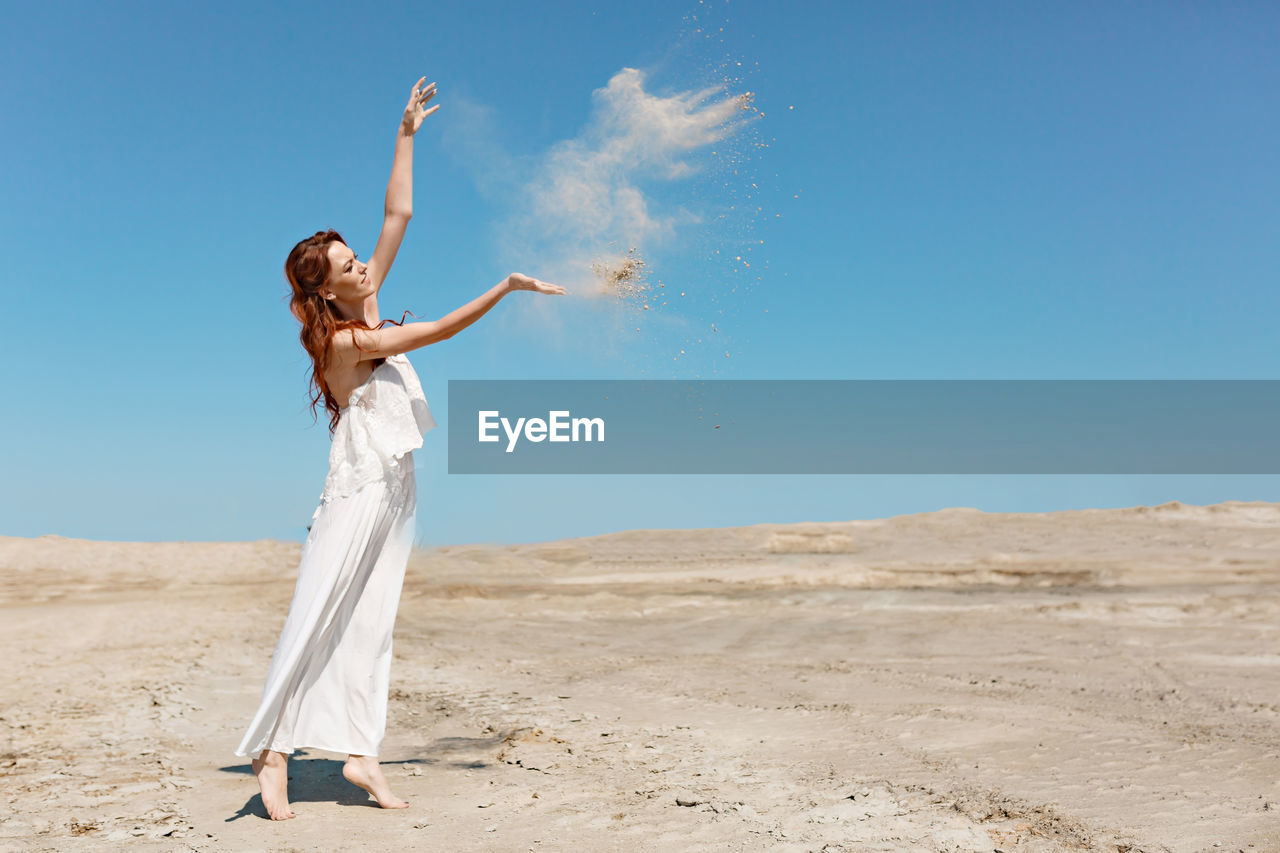 Woman with arms outstretched on sand against clear sky