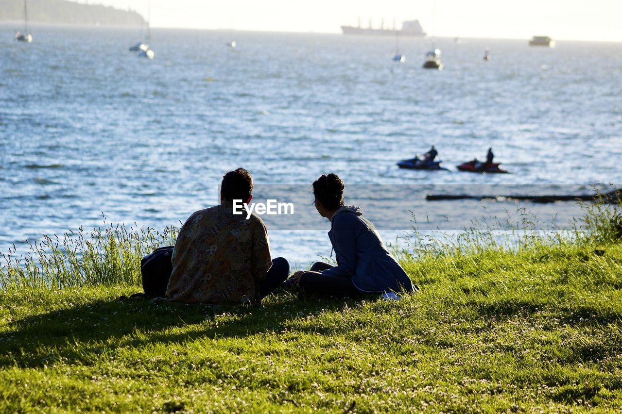 Friends sitting at beach against sky