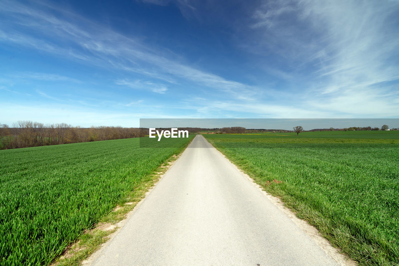 Empty road amidst field against sky