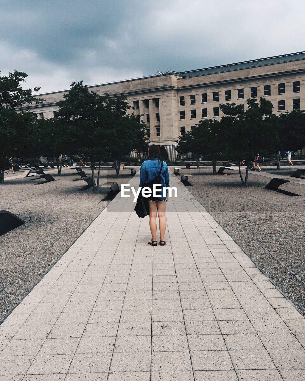 Full length rear view of woman standing footpath by building against sky