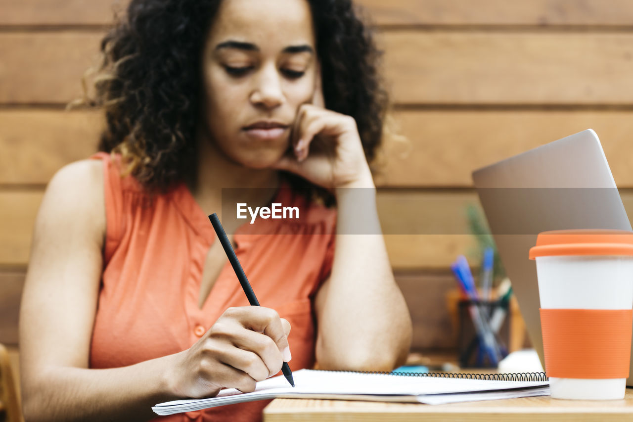 Woman writing on book while sitting at desk