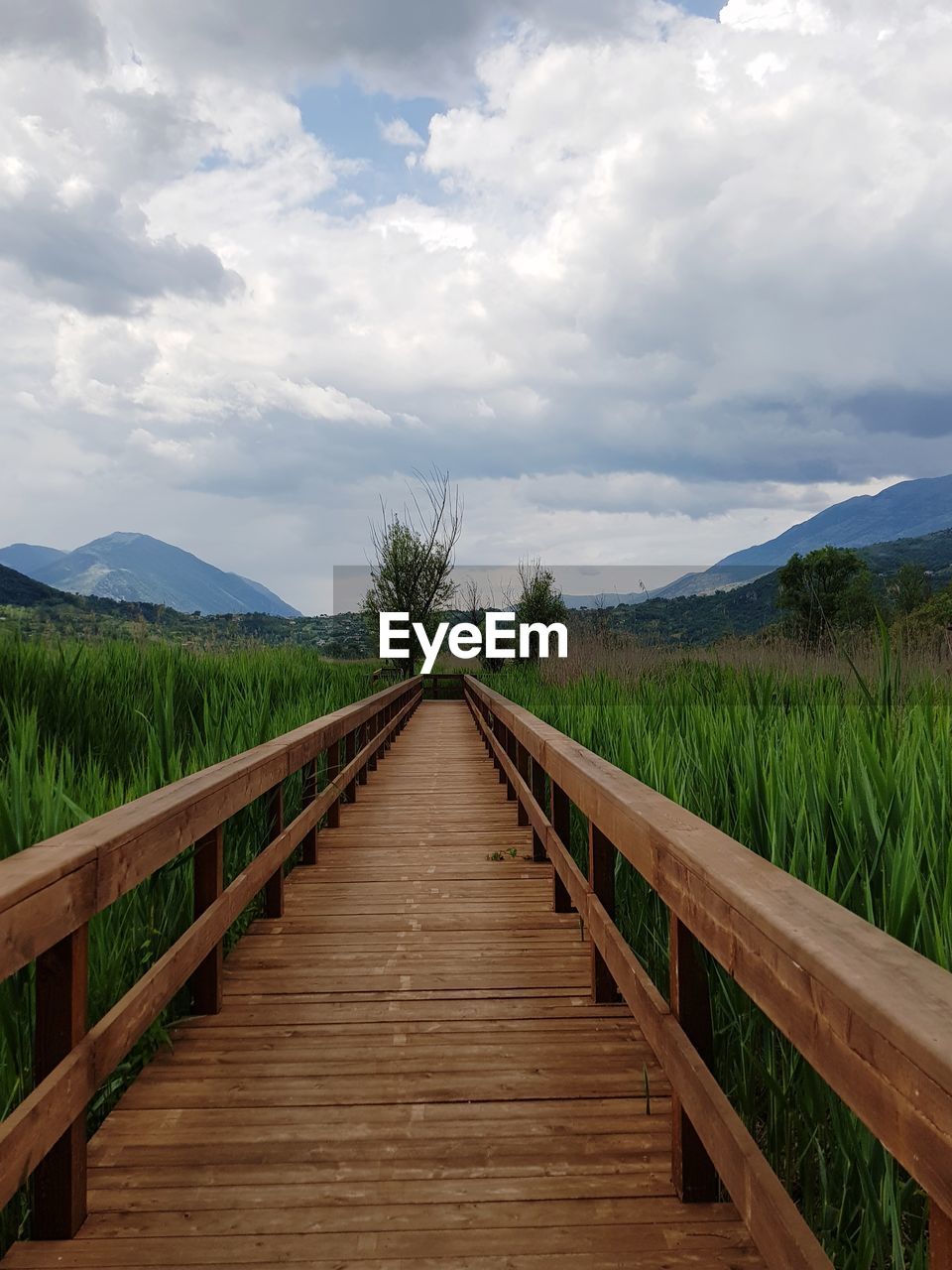 View of wooden boardwalk leading towards mountains against sky