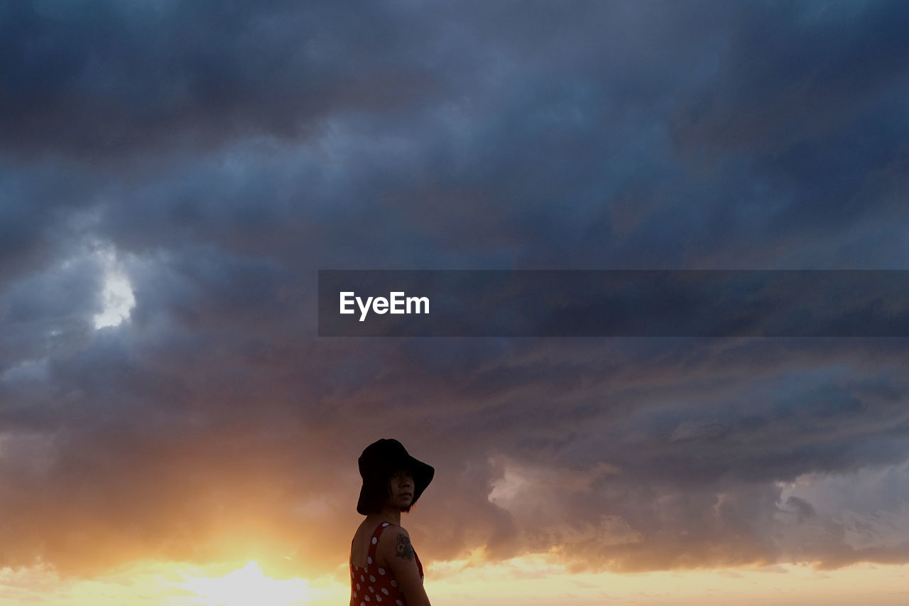 low angle view of woman standing on field against cloudy sky