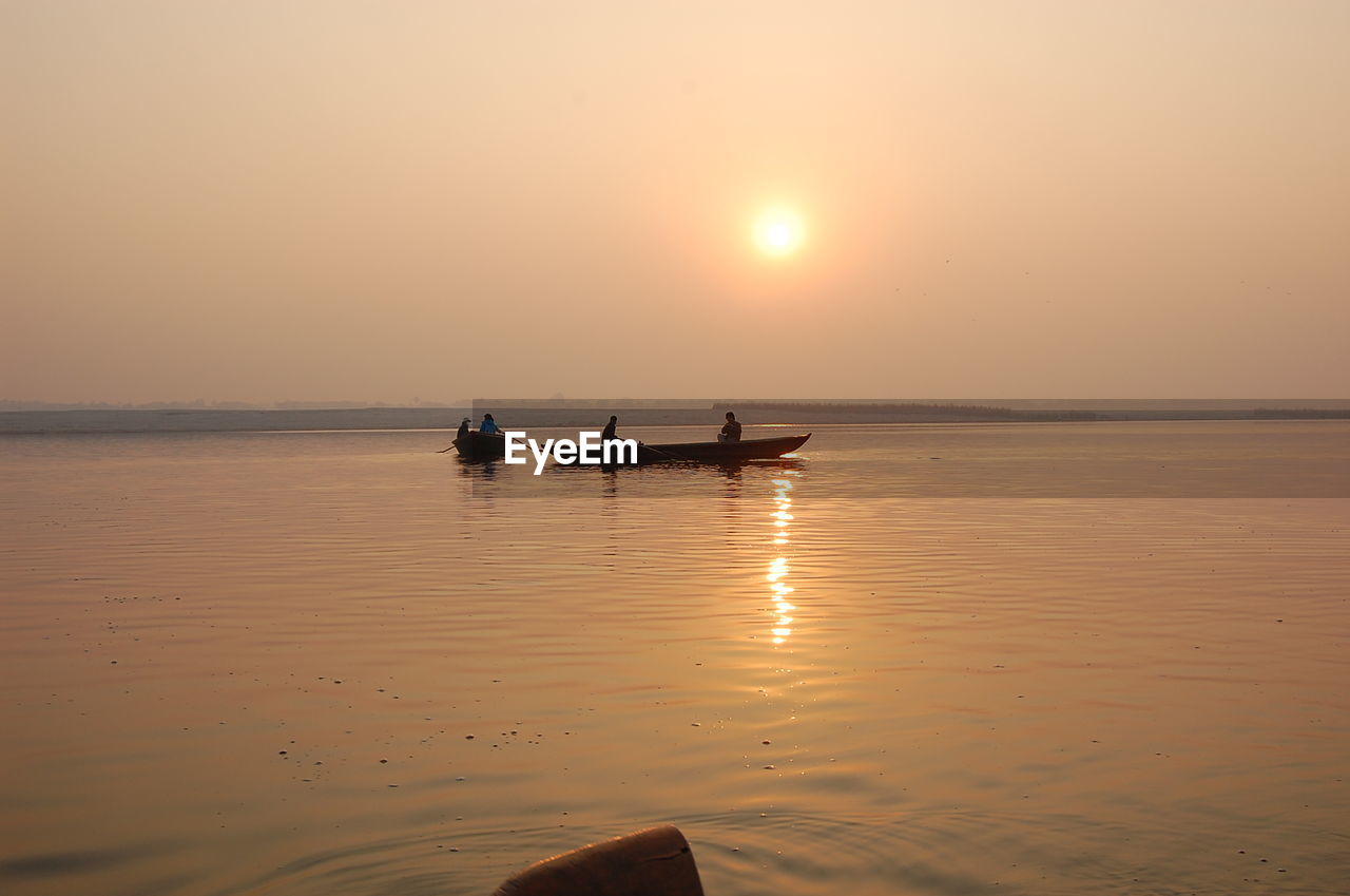 PEOPLE IN SEA AGAINST SKY DURING SUNSET