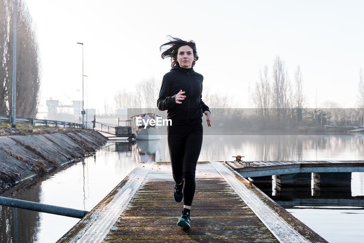Young adult woman is running on a harbor quay in the morning - health and wellness concept