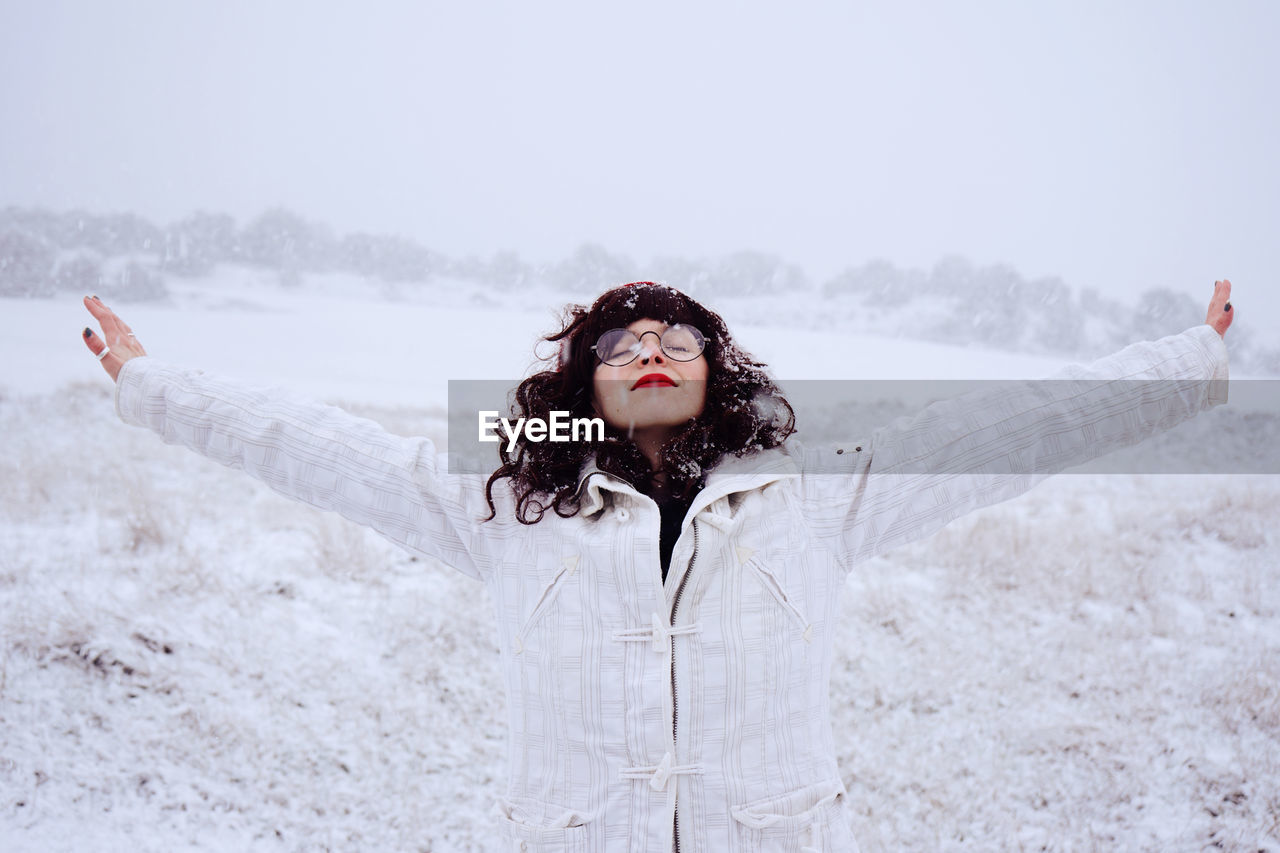 Young woman with arms outstretched standing on field during snowfall
