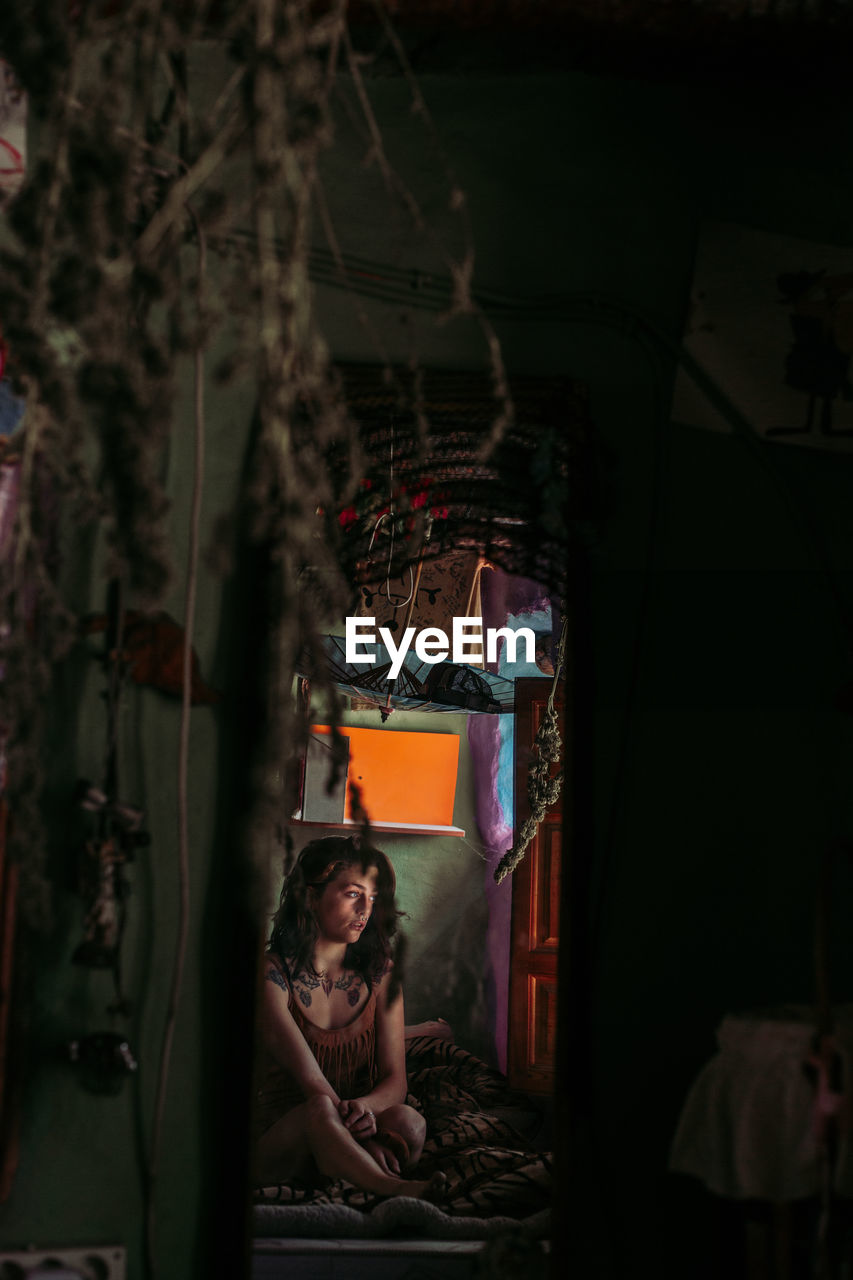 Female sitting on bedroom with plants hanging from ceiling