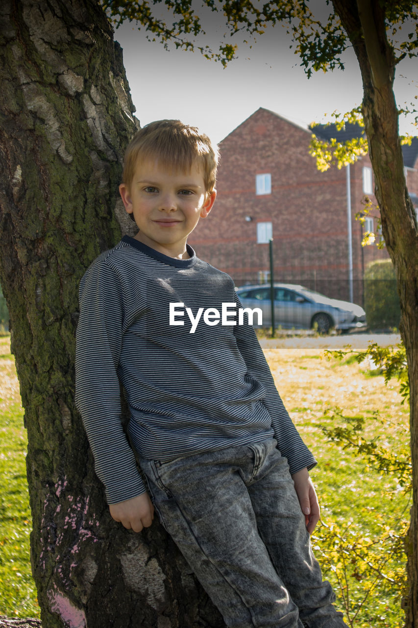 Portrait of smiling boy leaning on tree trunk in park