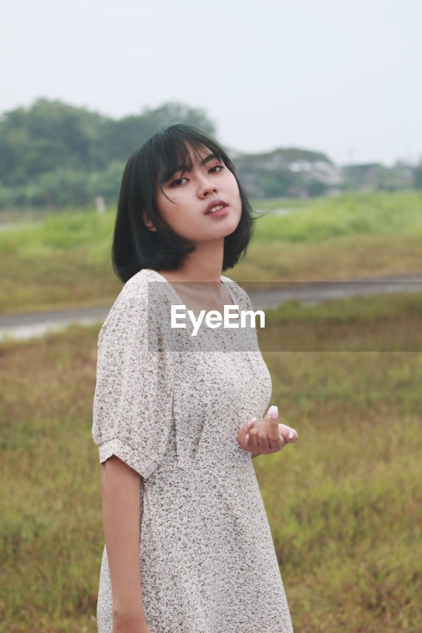 portrait of young woman standing on field against sky