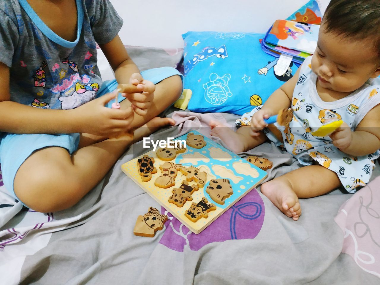 Siblings playing with toys on bed at home