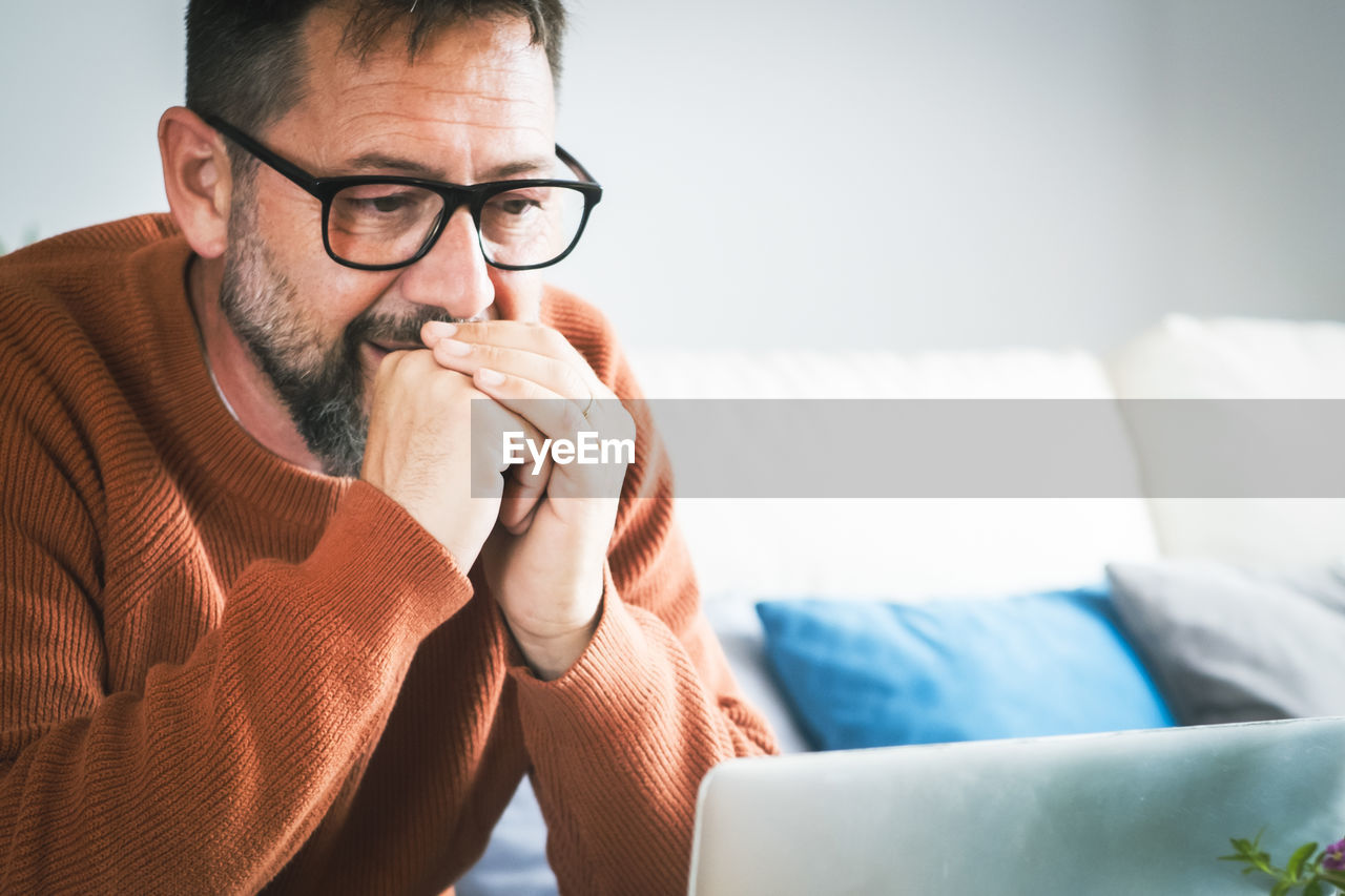 portrait of young man using mobile phone while lying on sofa at home