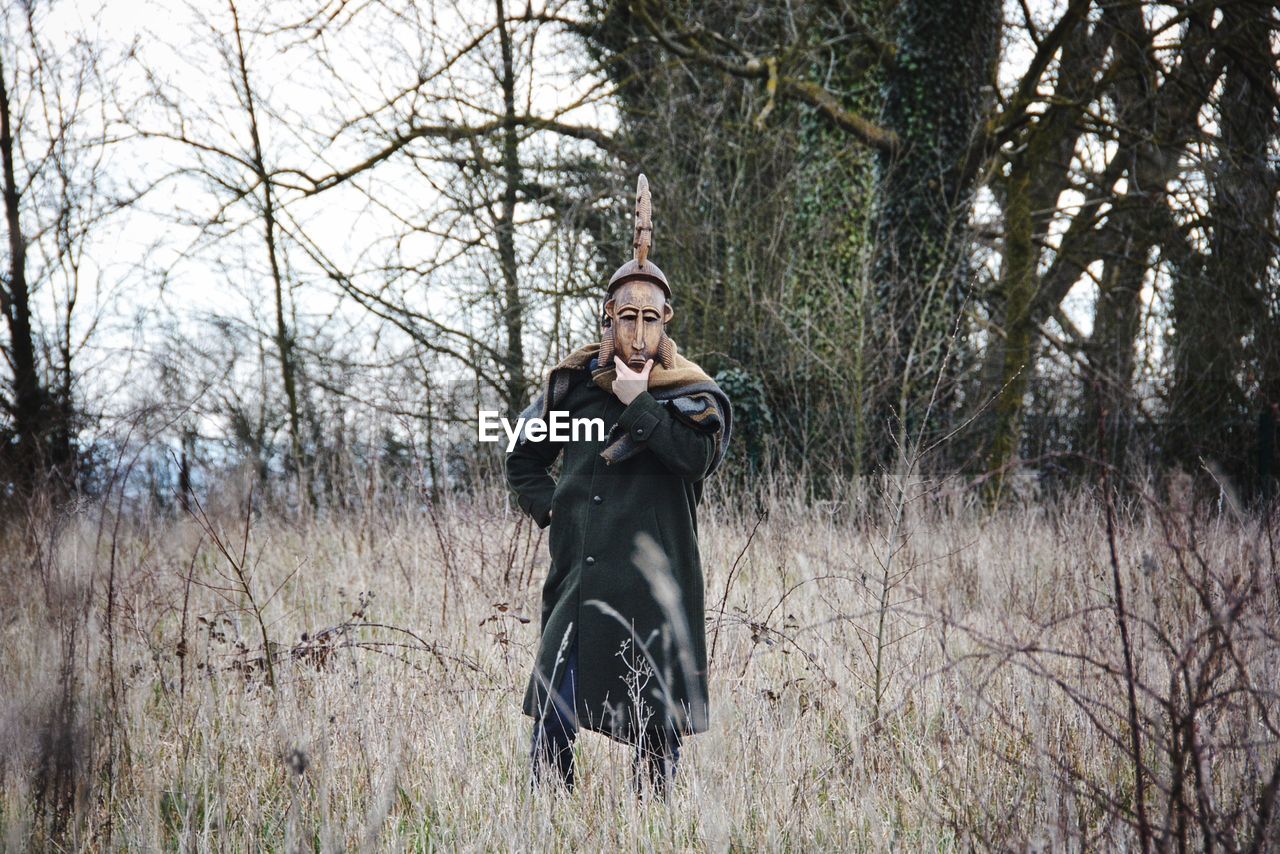 Man with mask standing by bare tree in forest